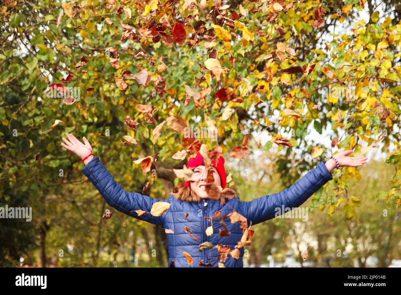 Défie les gens de l'automne. Jeune fille levant la main et jetant des feuilles. De nombreuses feuilles sèches orange, jaune, verte volantes. Profitez de l'automne. Bonne chute. Drôle Banque D'Images