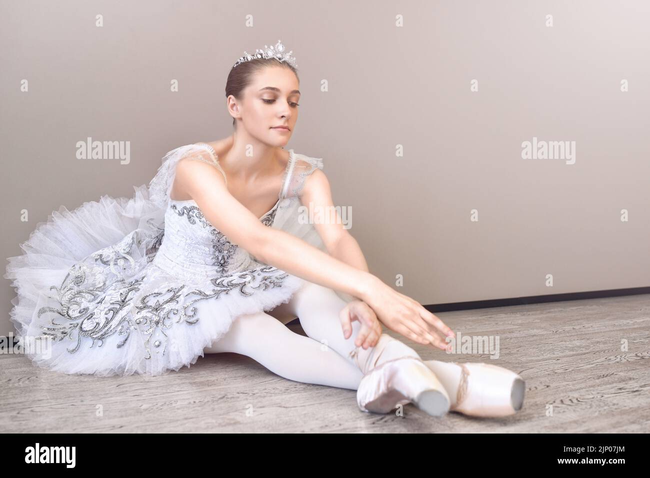 jolie ballerine assise sur le sol avec ses bras étirés vers l'avant, pratiquant des poses de ballet dans le studio Banque D'Images