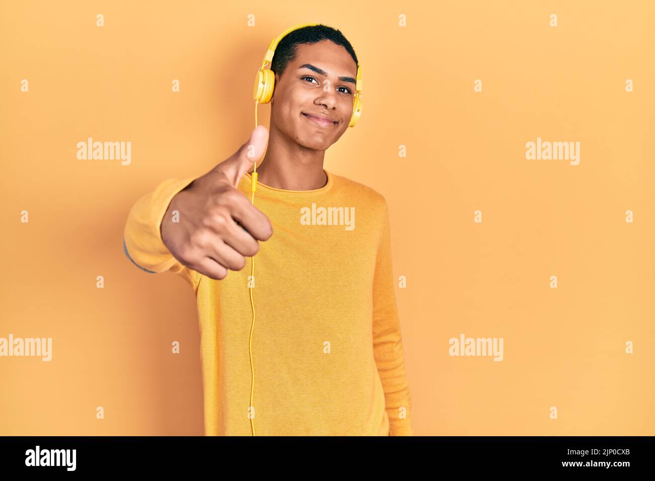 Jeune afro-américain qui écoute de la musique avec un casque, fait un geste de pouce heureux avec la main. Approuvant l'expression en regardant la caméra sho Banque D'Images