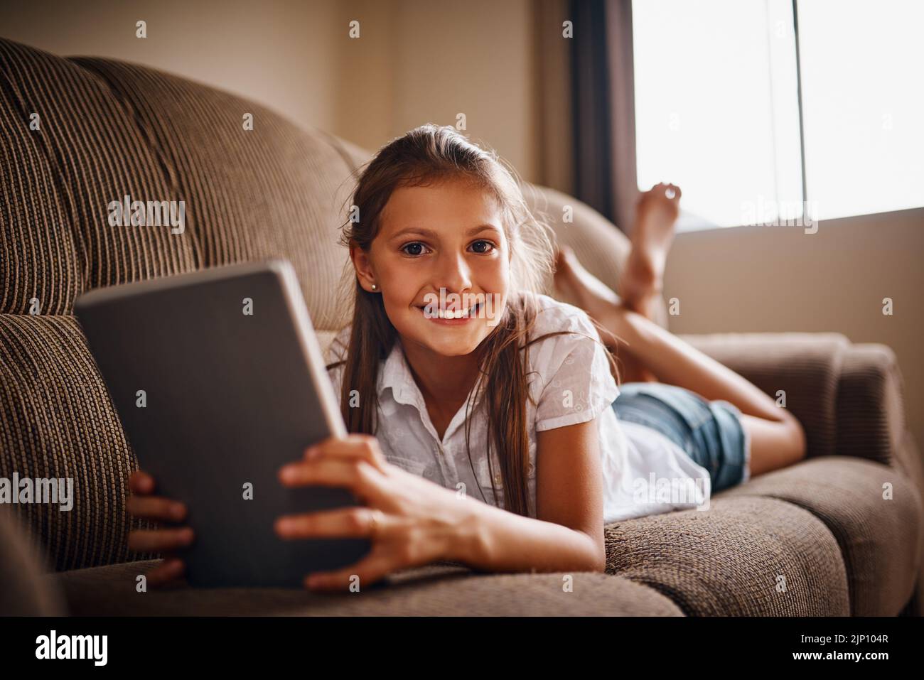 C'est ma partie préférée de la journée. Portrait complet d'une jeune fille utilisant sa tablette tout en étant allongé sur un canapé à la maison. Banque D'Images