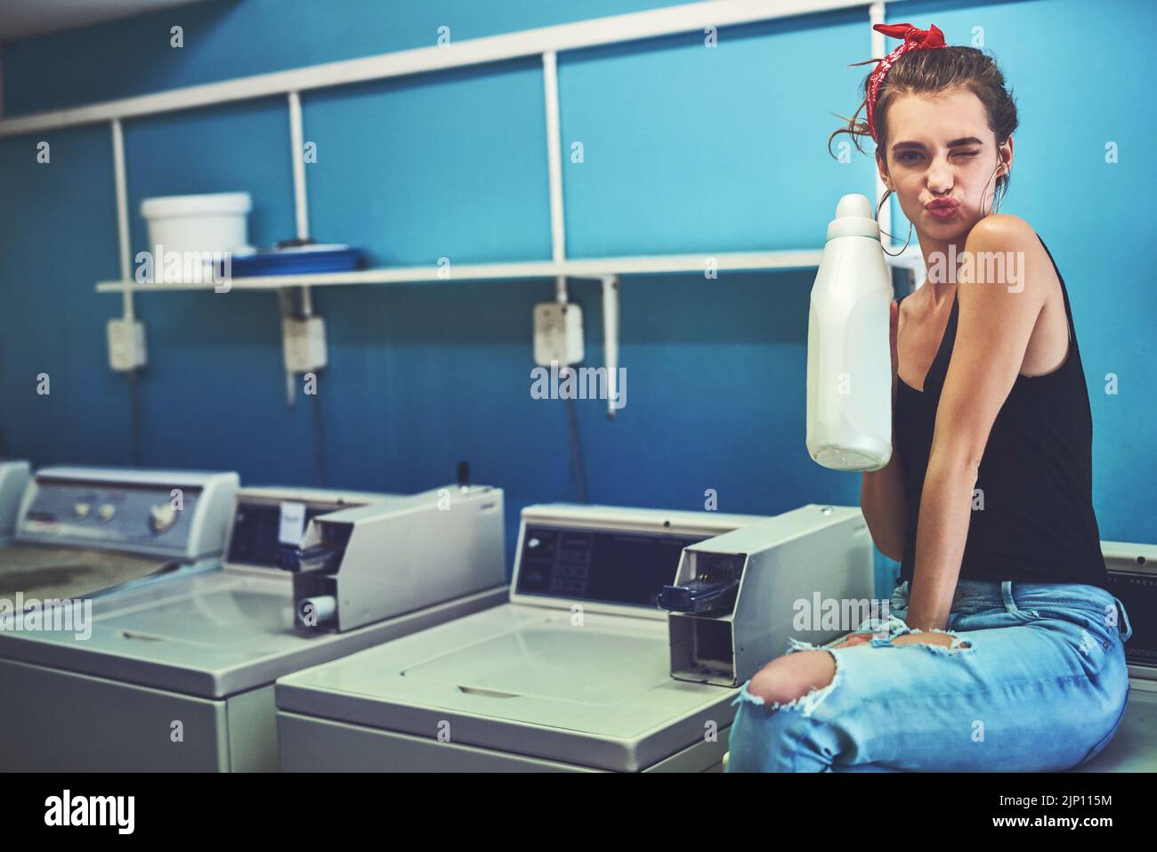 Passons au nettoyage. Portrait d'une jeune femme attirante assise sur une machine à laver tout en tenant l'eau de Javel pour laver son linge avec l'intérieur d'un linge Banque D'Images