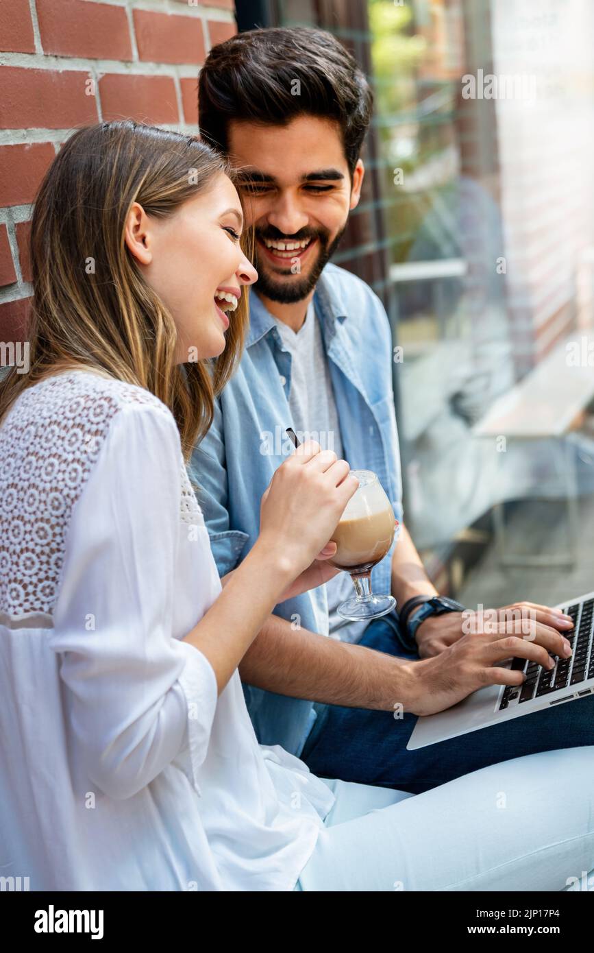 Couple assis au café souriant, en utilisant un ordinateur portable, passer du temps avec plaisir, boire du café. Banque D'Images
