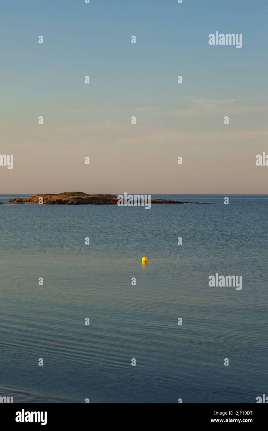 Une île basse est placée sur la mer bleue et calme. Une bouée jaune guide le regard vers l'île et le ciel bleu. L'atmosphère est calme et sereine zen. Banque D'Images