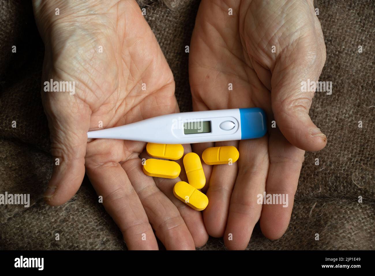 la femme désireuse tient un thermomètre électronique et des pilules dans ses mains sur le lit, de la fièvre et de la fièvre pendant une pandémie, la temperatuka sans poids, pensi malade Banque D'Images