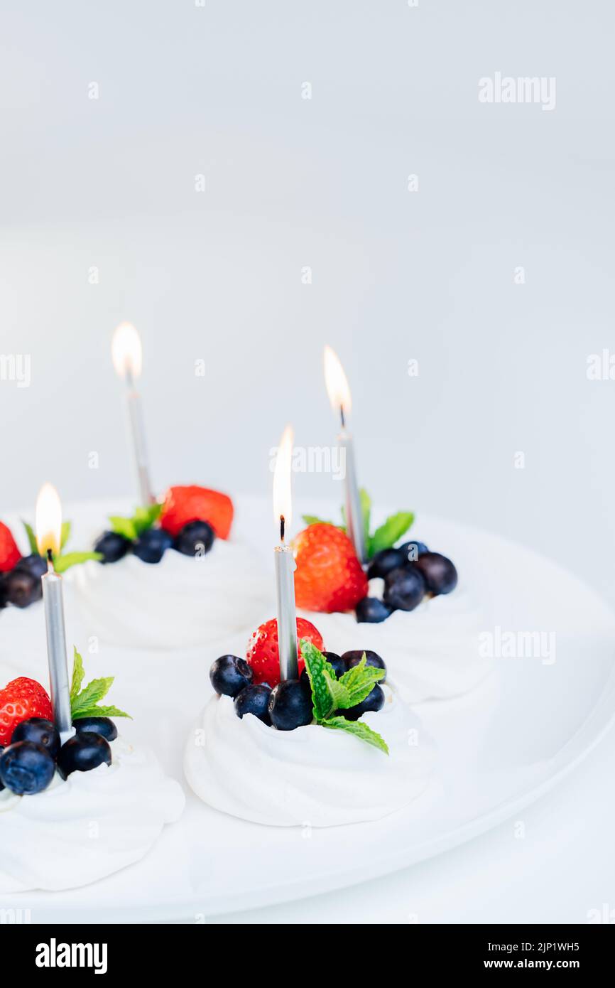 Dessert meringue le gâteau Pavlova se niche avec des fraises fraîches et des myrtilles avec de la menthe sur la plaque blanche avec des bougies allumées. Joyeux anniversaire gâteau ide Banque D'Images Dessert meringue le gâteau Pavlova se niche avec des fraises fraîches et des myrtilles avec de la menthe sur la plaque blanche avec des bougies allumées. Joyeux anniversaire gâteau ide Banque D'Images