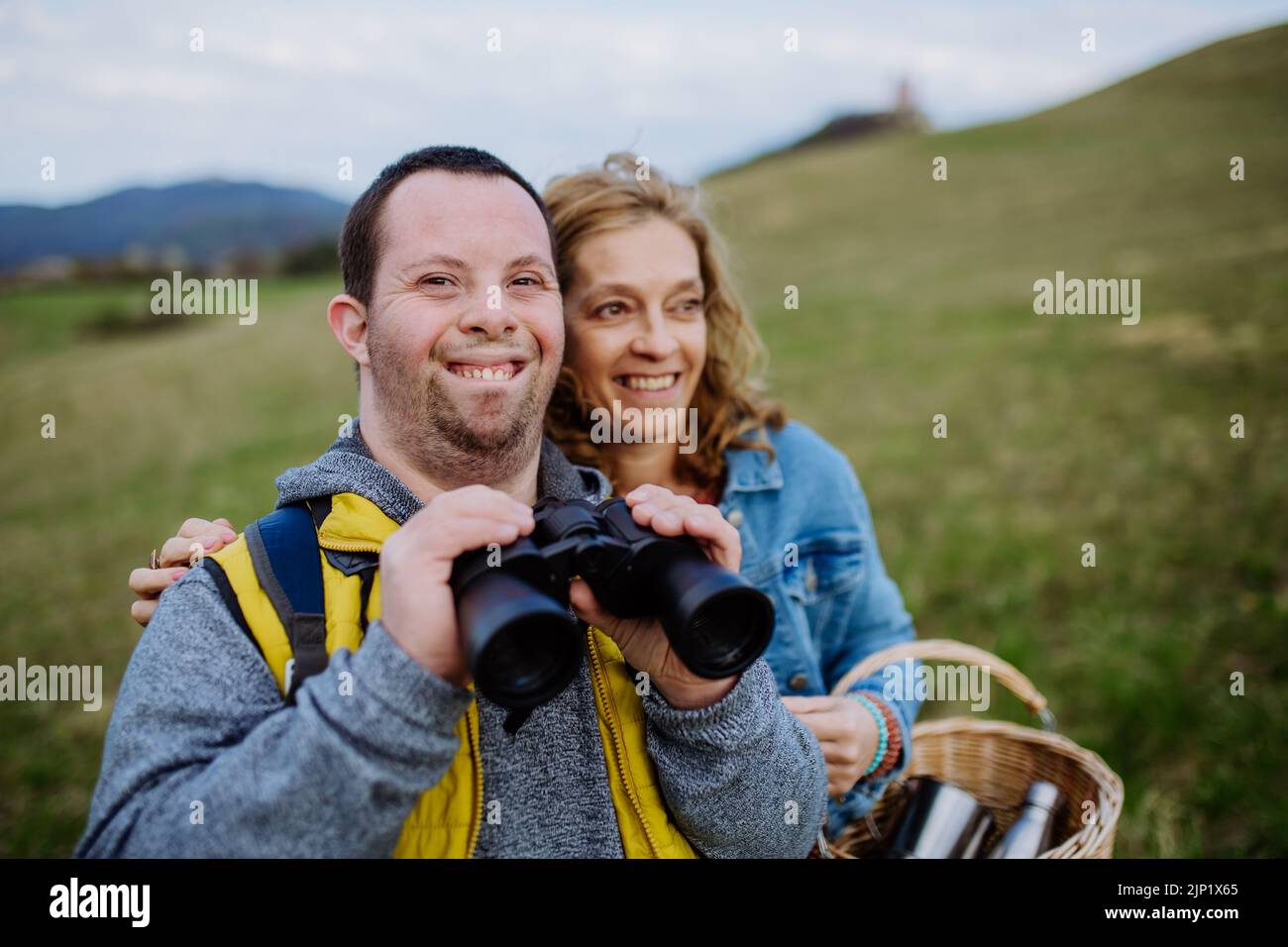 Jeune homme heureux avec le syndrome de Down avec sa mère se reposant dans la nature, assis et regardant à travers des jumelles. Banque D'Images