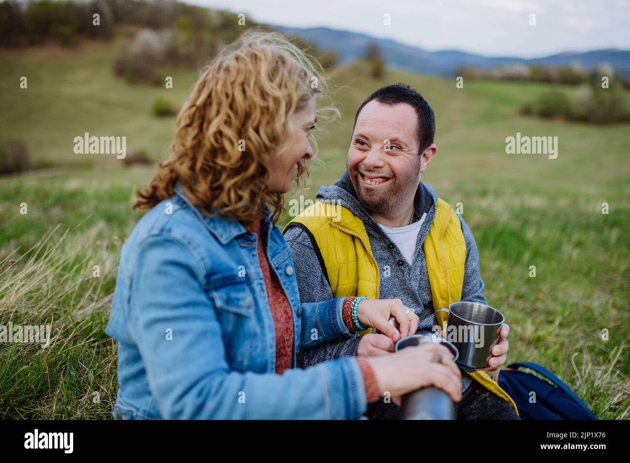 Portrait du jeune homme heureux avec le syndrome de Down avec sa mère se reposant dans la nature, assis et regardant la vue. Banque D'Images