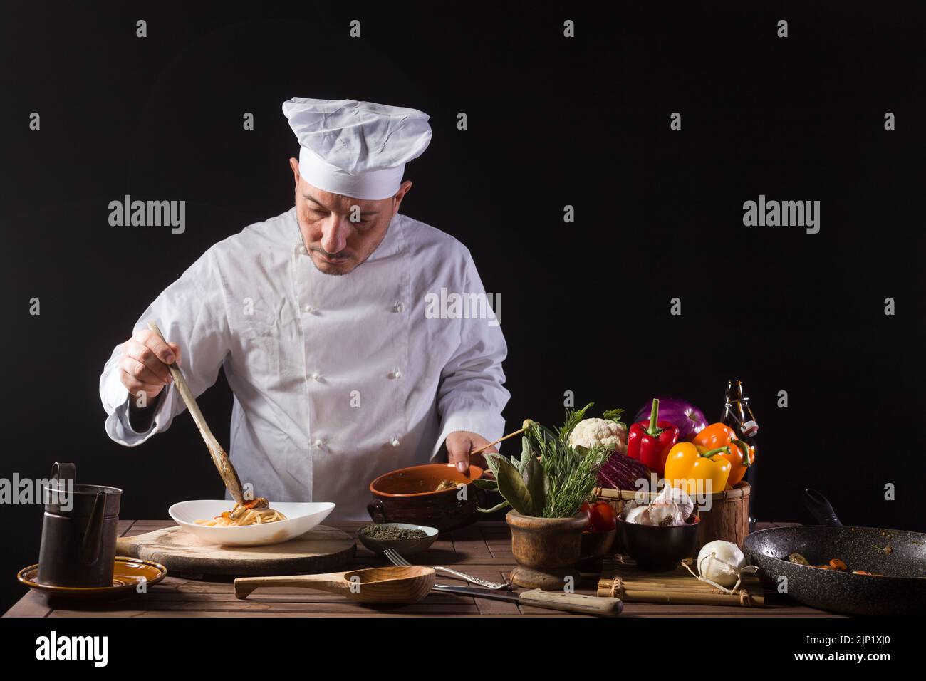 Le chef masculin en uniforme blanc prépare des spaghetti aux légumes sur le plat avant de servir tout en travaillant dans une cuisine de restaurant Banque D'Images