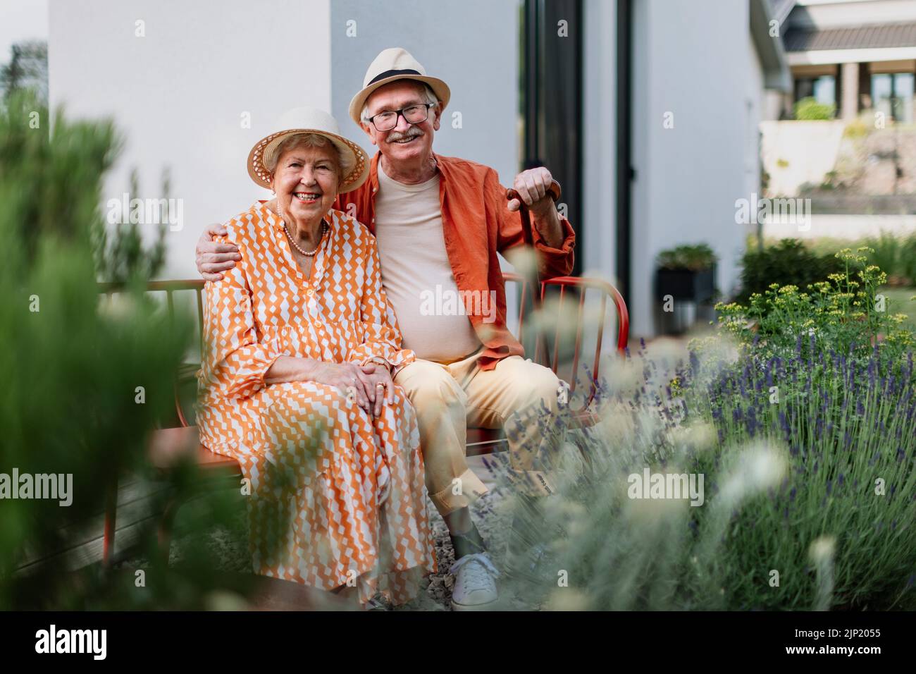 Heureux couple senior assis ensemble dans le banc de jardin, souriant et regardant la caméra. Banque D'Images