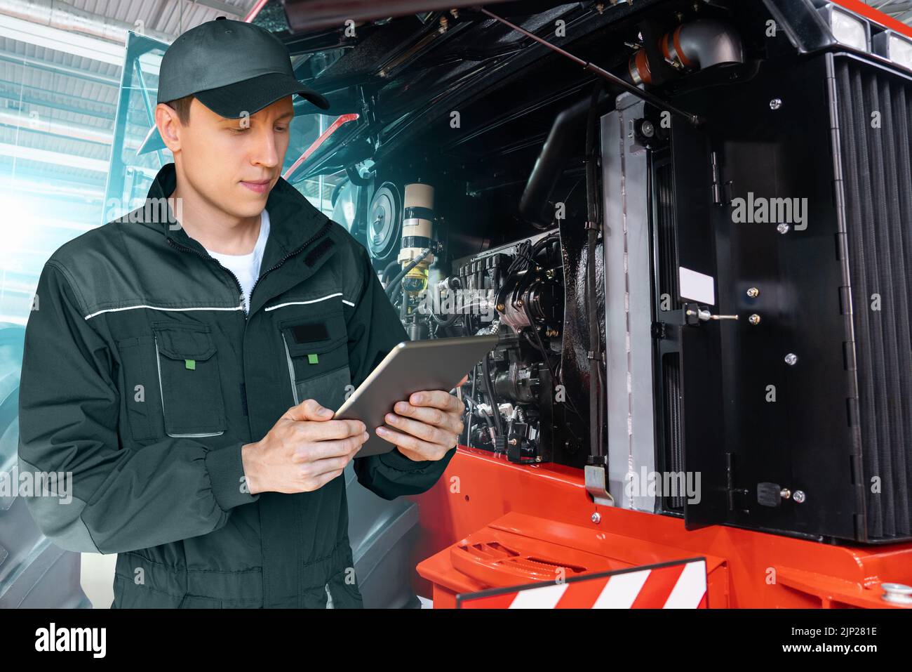Technicien de maintenance avec tablette numérique sur un arrière-plan du tracteur avec capot ouvert Banque D'Images