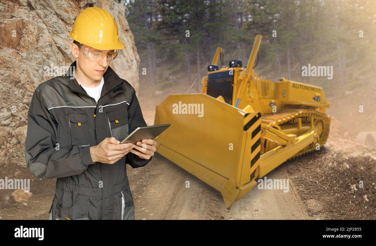 L'ingénieur programme un bulldozer autonome à l'aide d'une tablette numérique Banque D'Images