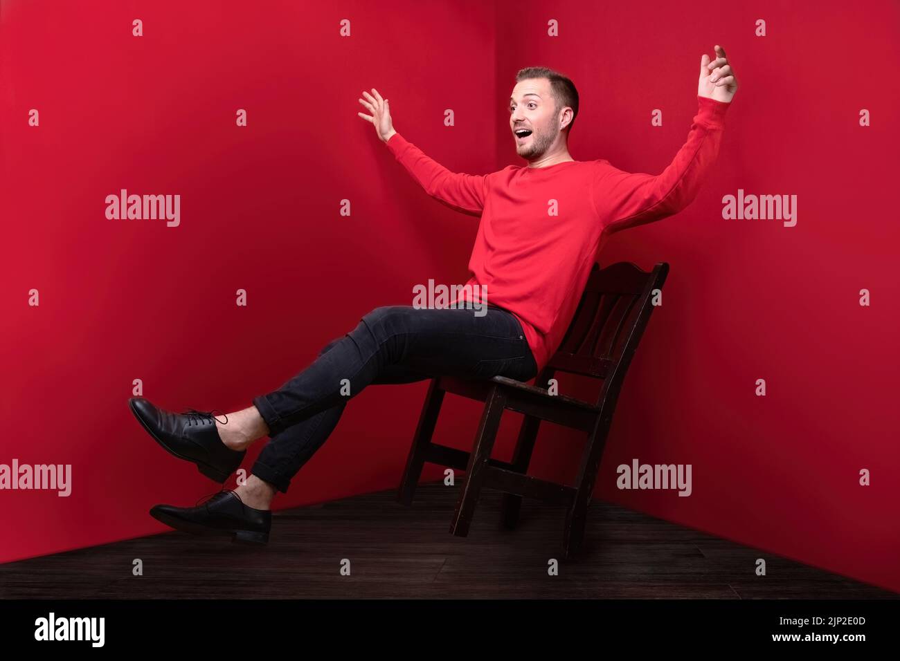 Un homme en rouge montrant la chute d'une chaise avec les mains larges ouvertes Banque D'Images