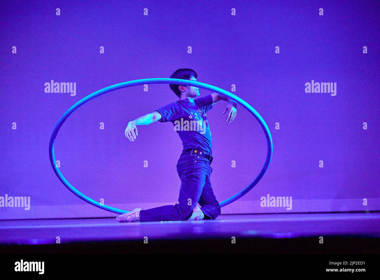 Un danseur de ballet contemporain s'agenouillait au milieu d'un panier sur une scène à fond violet Banque D'Images