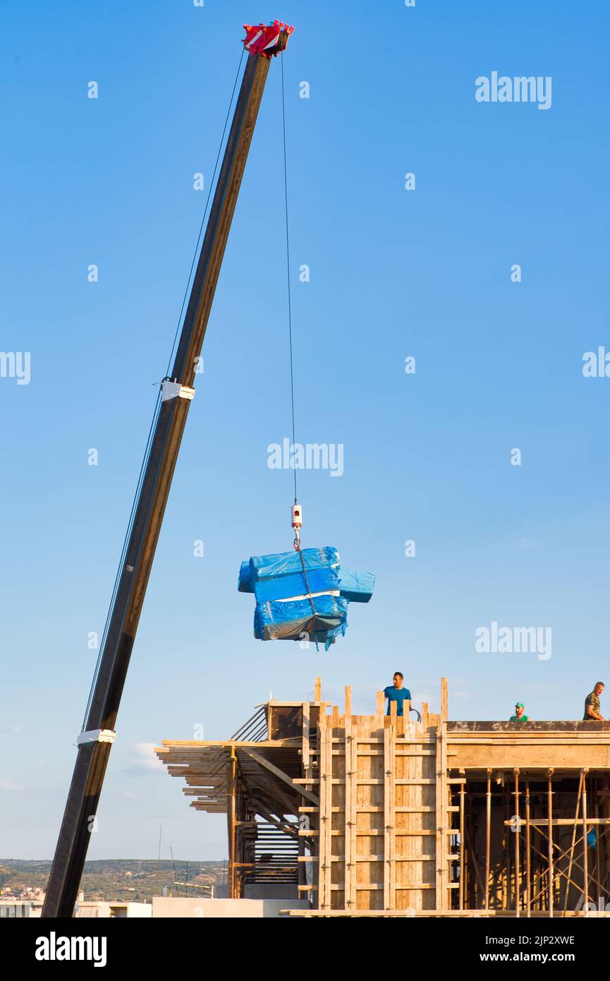 les ouvriers de la construction déchargent les matériaux de construction d'une grue Banque D'Images