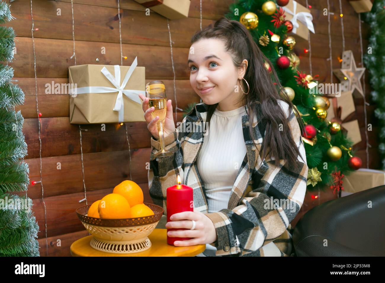 Fille en vêtements décontractés avec un verre de champagne près de l'arbre de Noël. Banque D'Images