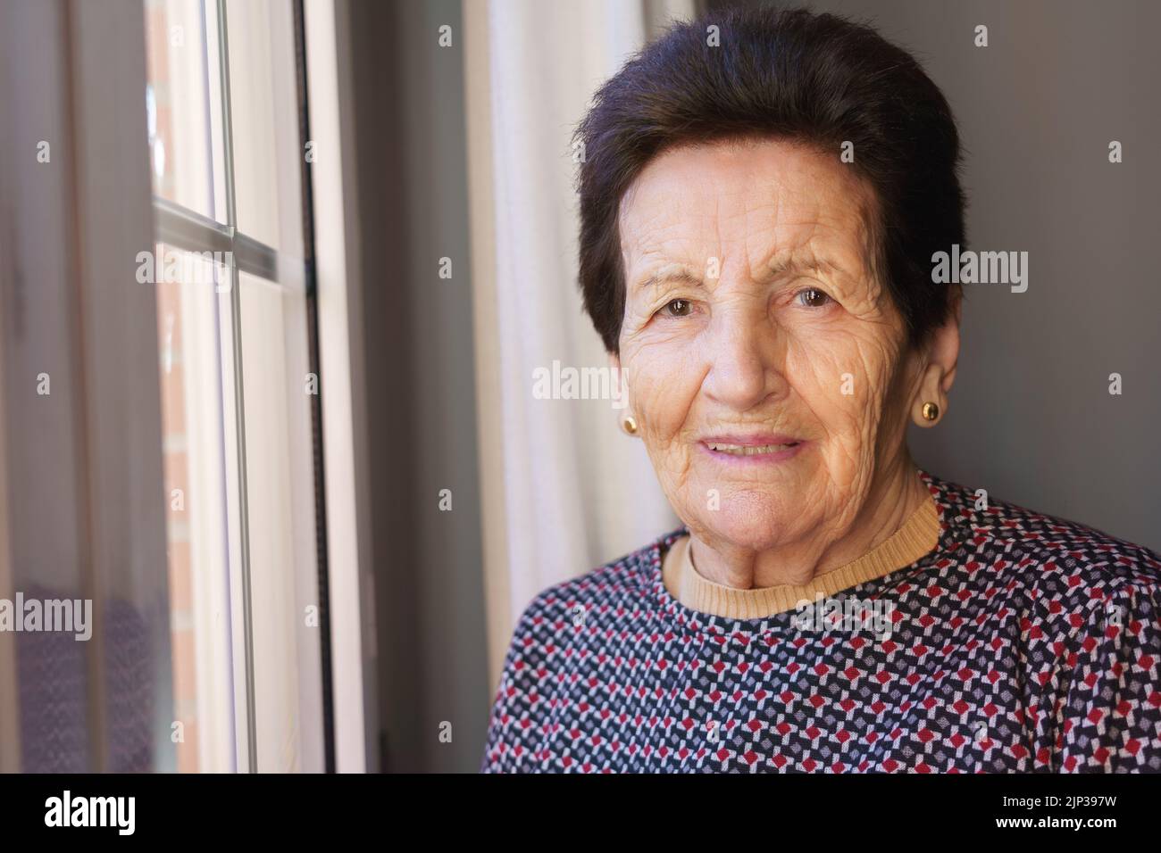 femme blanche de 90 ans à côté de la fenêtre riant Banque D'Images