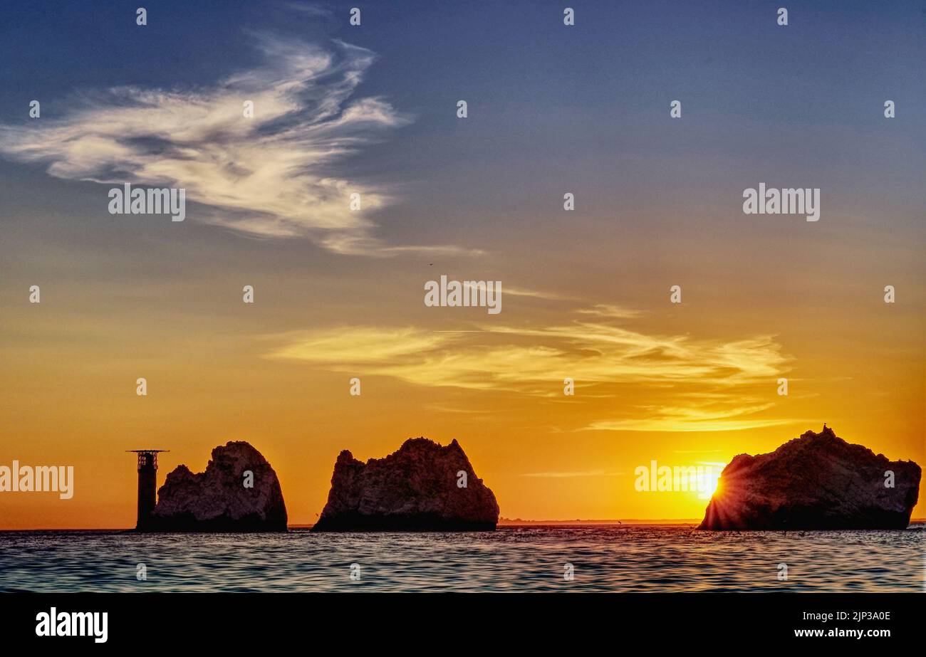 Le soleil se coucher derrière l'une des piles de pierres au phare de Needles sur l'île de Wight. Le ciel montre quelques nuages d'été légers. Banque D'Images