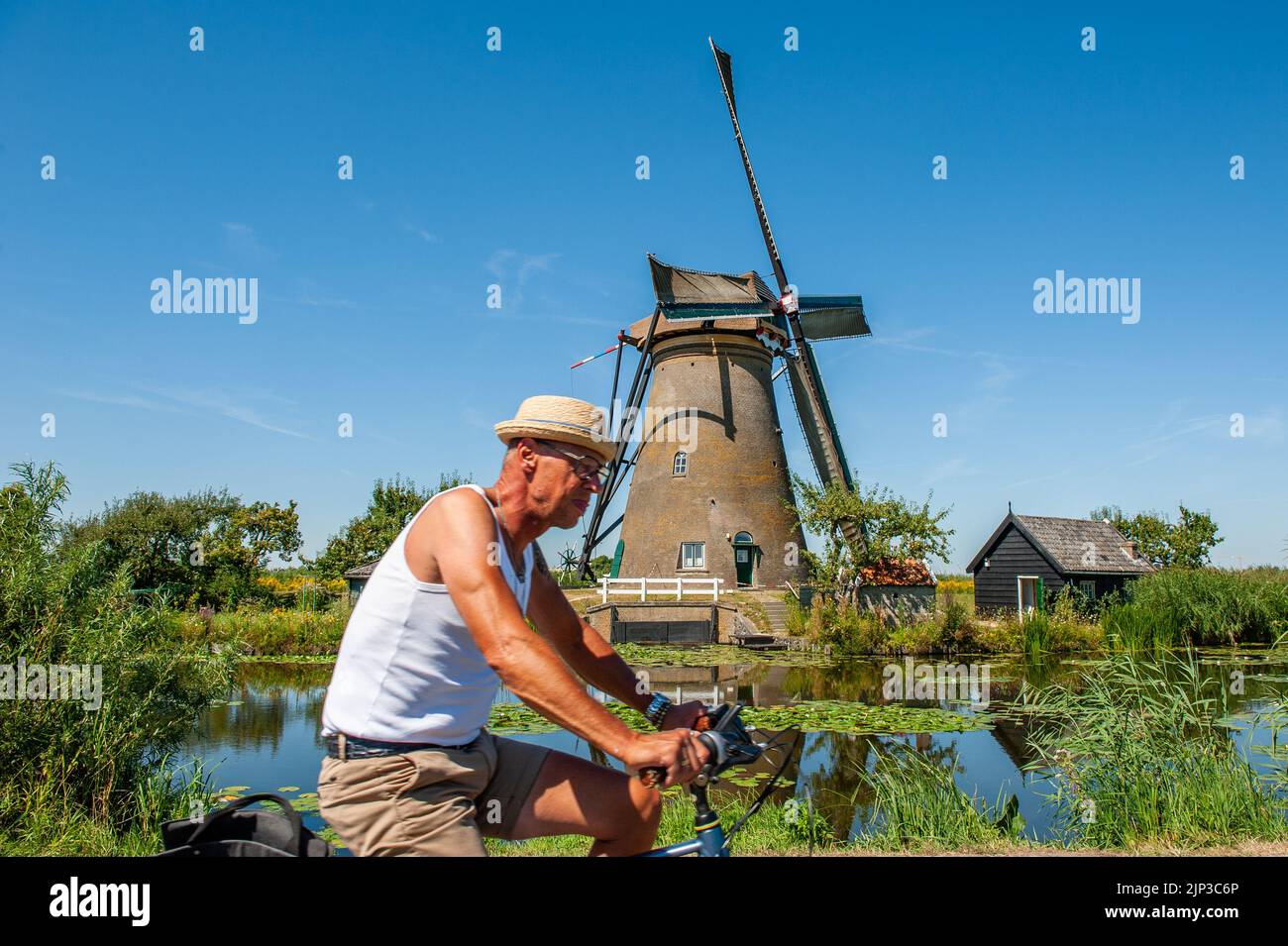Kinderdijk, pays-Bas. 13th août 2022. Un homme est vu passer sur son vélo devant l'un des moulins à vent. Dans la belle région riche en eau près de Dordrecht, vous trouverez les moulins à vent de Kinderdijk. Construits vers 1740, ces 19 magnifiques moulins à vent font partie d'un plus grand système de gestion de l'eau pour éviter les inondations. Aujourd'hui, ils symbolisent la gestion de l'eau aux pays-Bas et, en 1997, ils ont été déclarés site du patrimoine mondial de l'UNESCO. Chaque année, des milliers de touristes du monde entier visitent ce lieu emblématique. Crédit : SOPA Images Limited/Alamy Live News Banque D'Images
