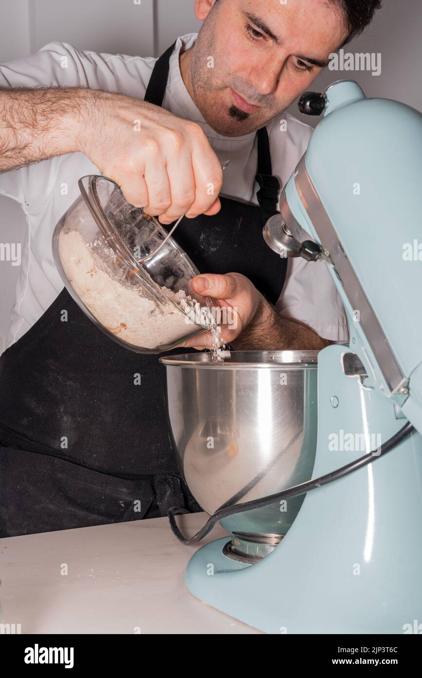 Un boulanger cuisant un gâteau de velours rouge en ajoutant de la poudre de cacao mélangée à la farine et à la levure dans le robot de cuisine, travailler dans la cuisine à la maison Banque D'Images