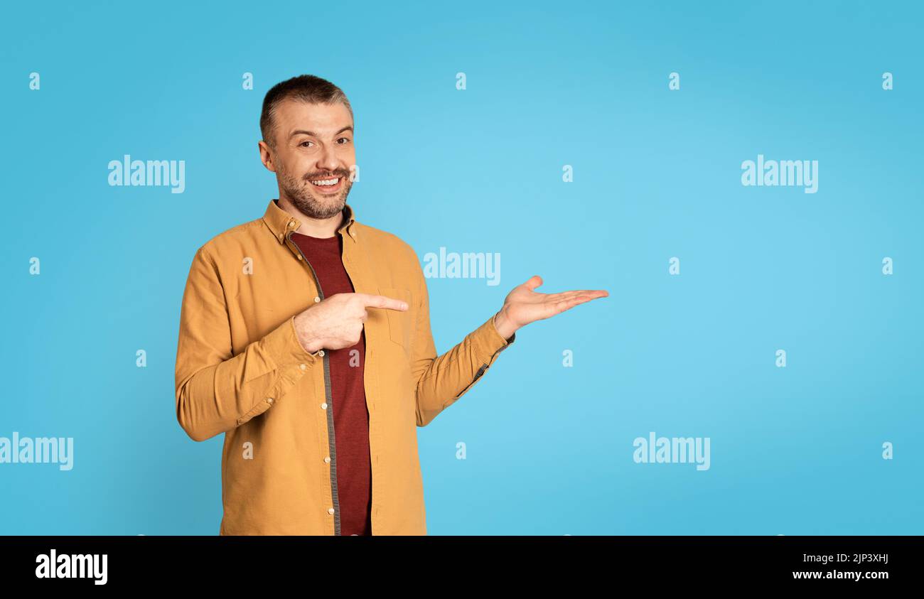 Homme d'âge moyen pointant le doigt vers sa main, fond bleu Banque D'Images