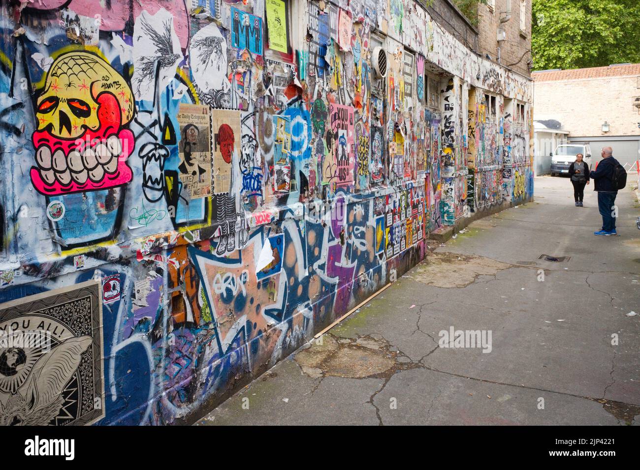 Deux photographes regardant un mur d'images graffitti au large de Brick Lane, Londres Banque D'Images