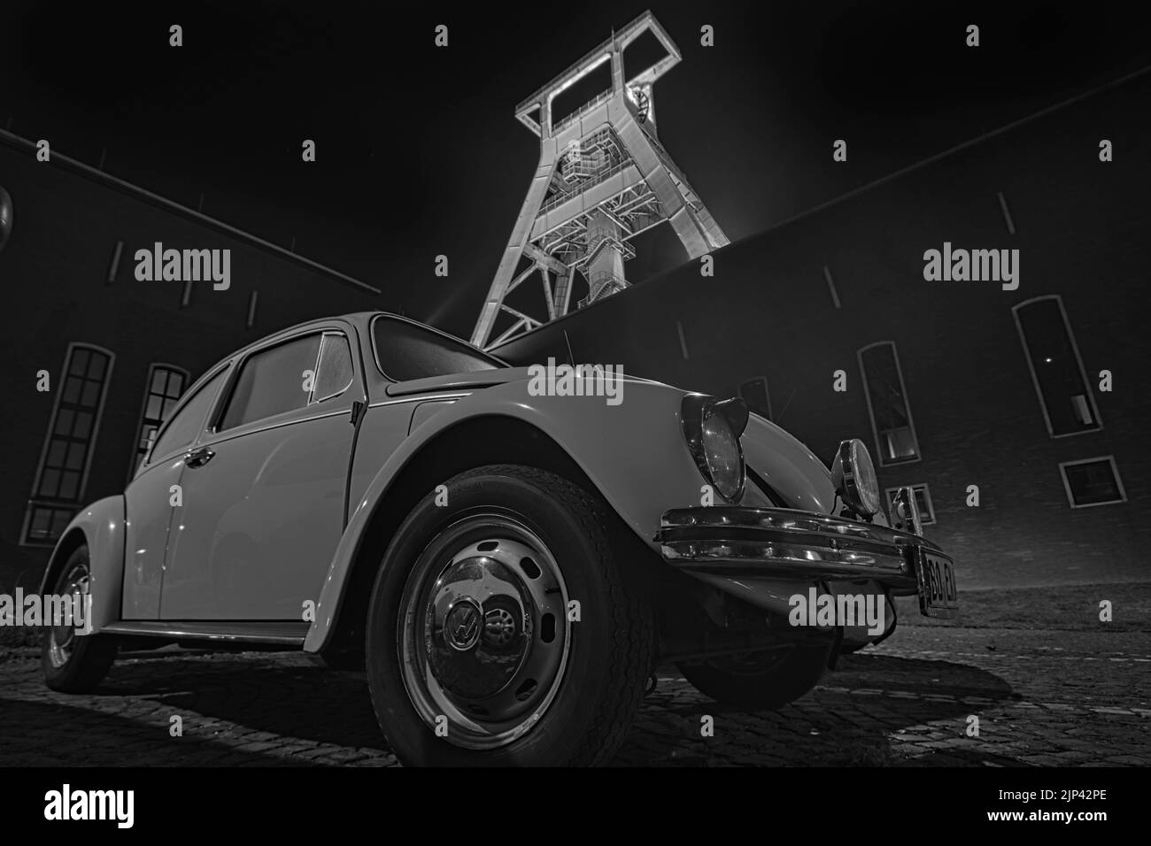 Échelle de gris à faible angle d'un vieux coléoptère VW devant un ancien convoyeur minier à Bochum Banque D'Images