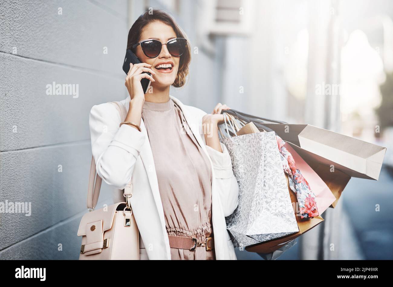 Femme de shopping insouciante et excitée lors d'un appel téléphonique tenant des sacs à l'extérieur dans la ville. Élégante, tendance et riche femme appréciant son week-end pendant Banque D'Images
