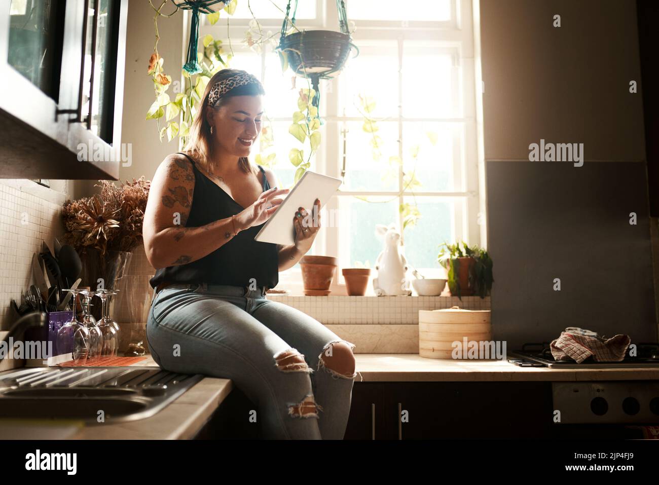 Une femme tendance qui navigue sur Internet sur une tablette en utilisant son nouveau wi-fi à la maison a l'air heureuse et satisfaite. Normal, réel et branché jeune femme recherche en ligne Banque D'Images