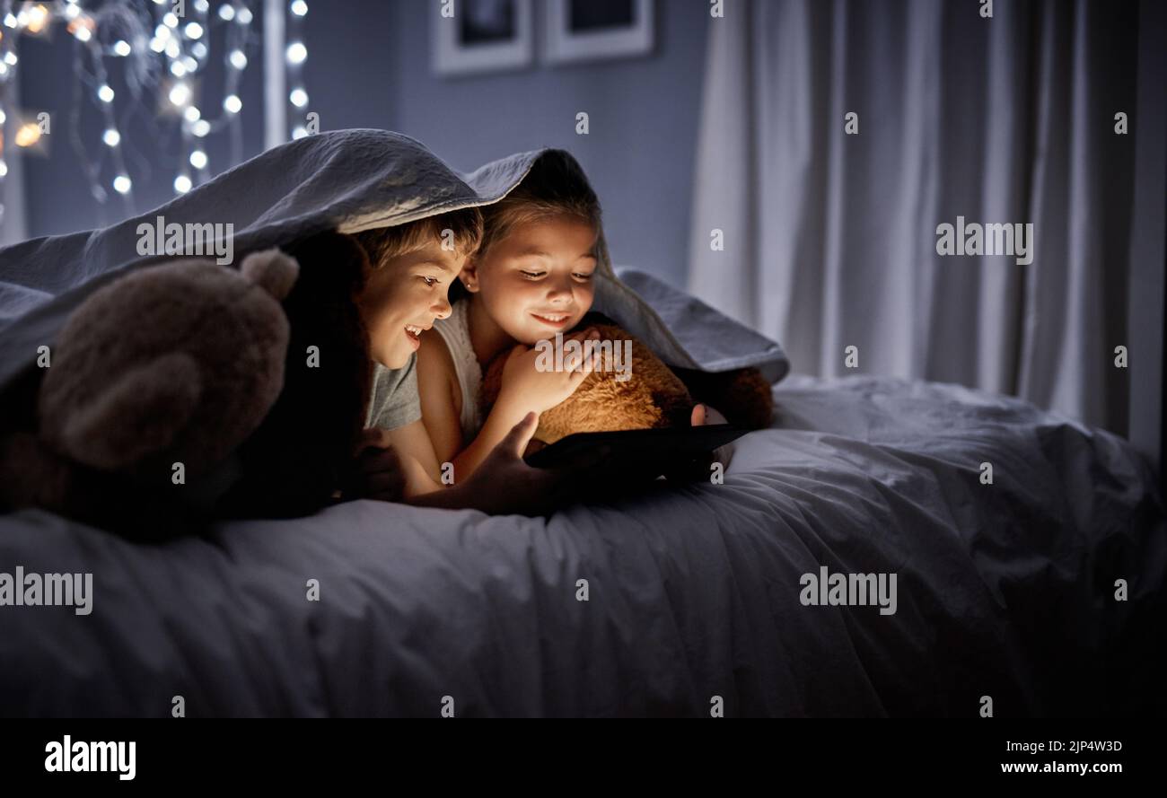 Jouer à leurs applications de jeu préférées. Deux adorables petits frères et sœurs utilisant une tablette numérique ensemble dans le lit la nuit. Banque D'Images