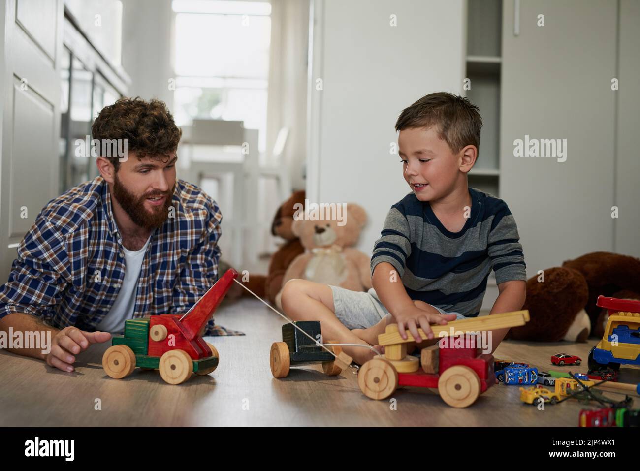 Comme le père, comme le fils. Un beau jeune homme et son fils jouant avec des jouets sur le plancher de la chambre. Banque D'Images