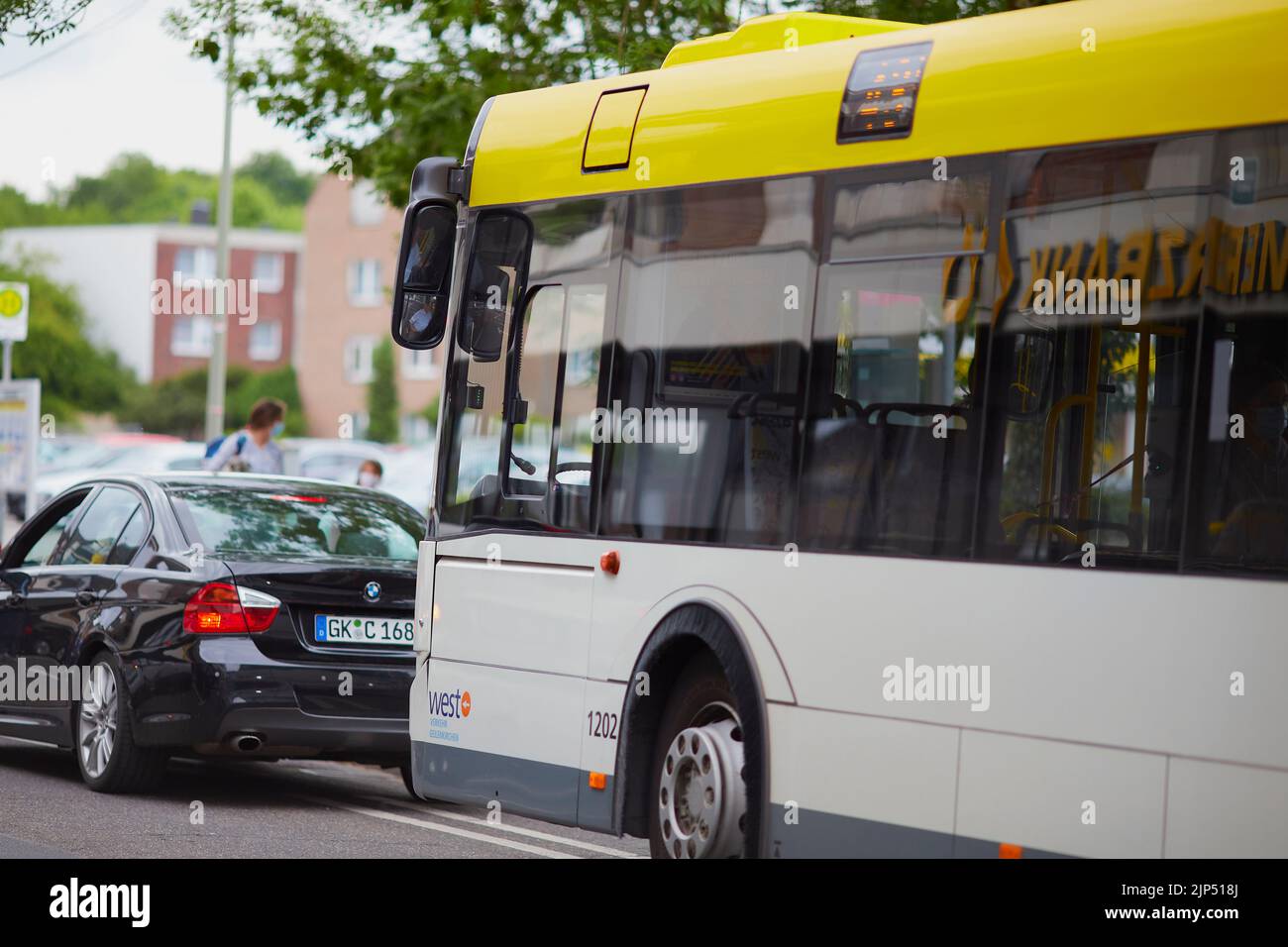 Un bus jaune et une voiture BMW devant lui conduisant dans une rue en journée à Geilenkirchen, en Allemagne Banque D'Images