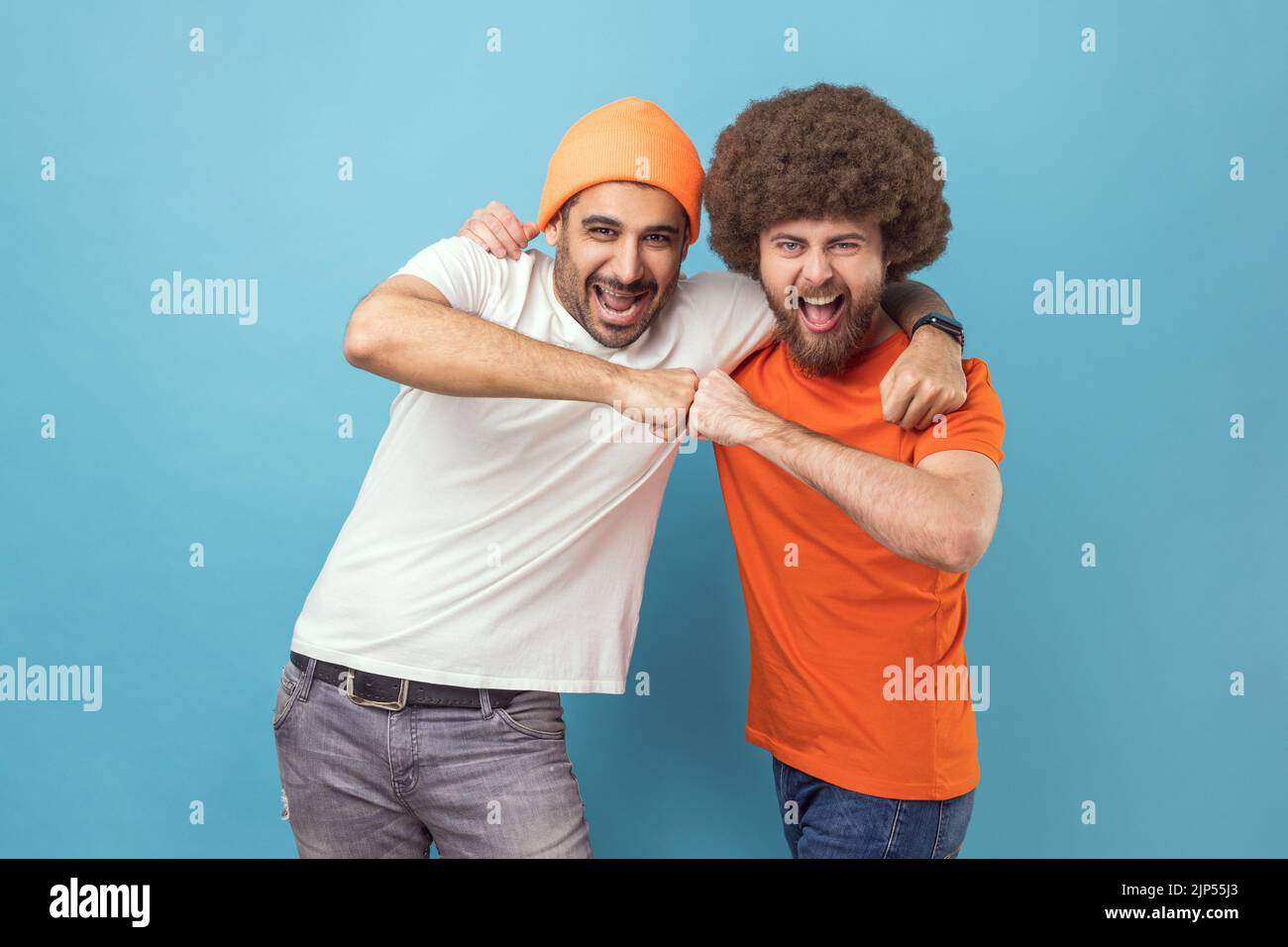 Oui. Portrait de deux beaux heureux jeunes adultes excités hipster hommes célébrant le triomphe ensemble, montrant le poing du bro, le pouvoir cinq signe. Studio d'intérieur isolé sur fond bleu. Banque D'Images
