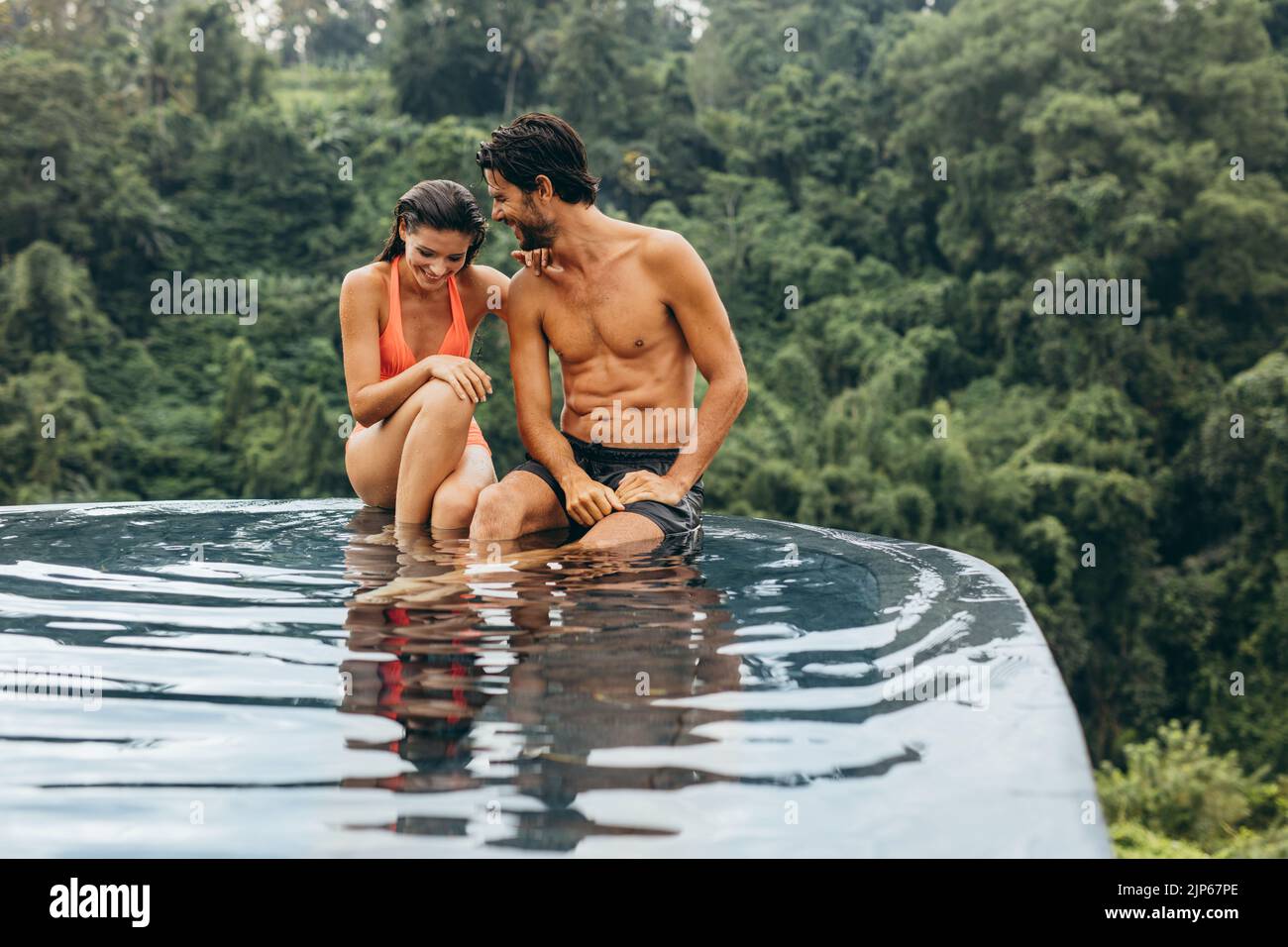 Un jeune couple heureux se détendant au bord de la piscine extérieure. Jeune homme et femme aimant en vacances. Banque D'Images