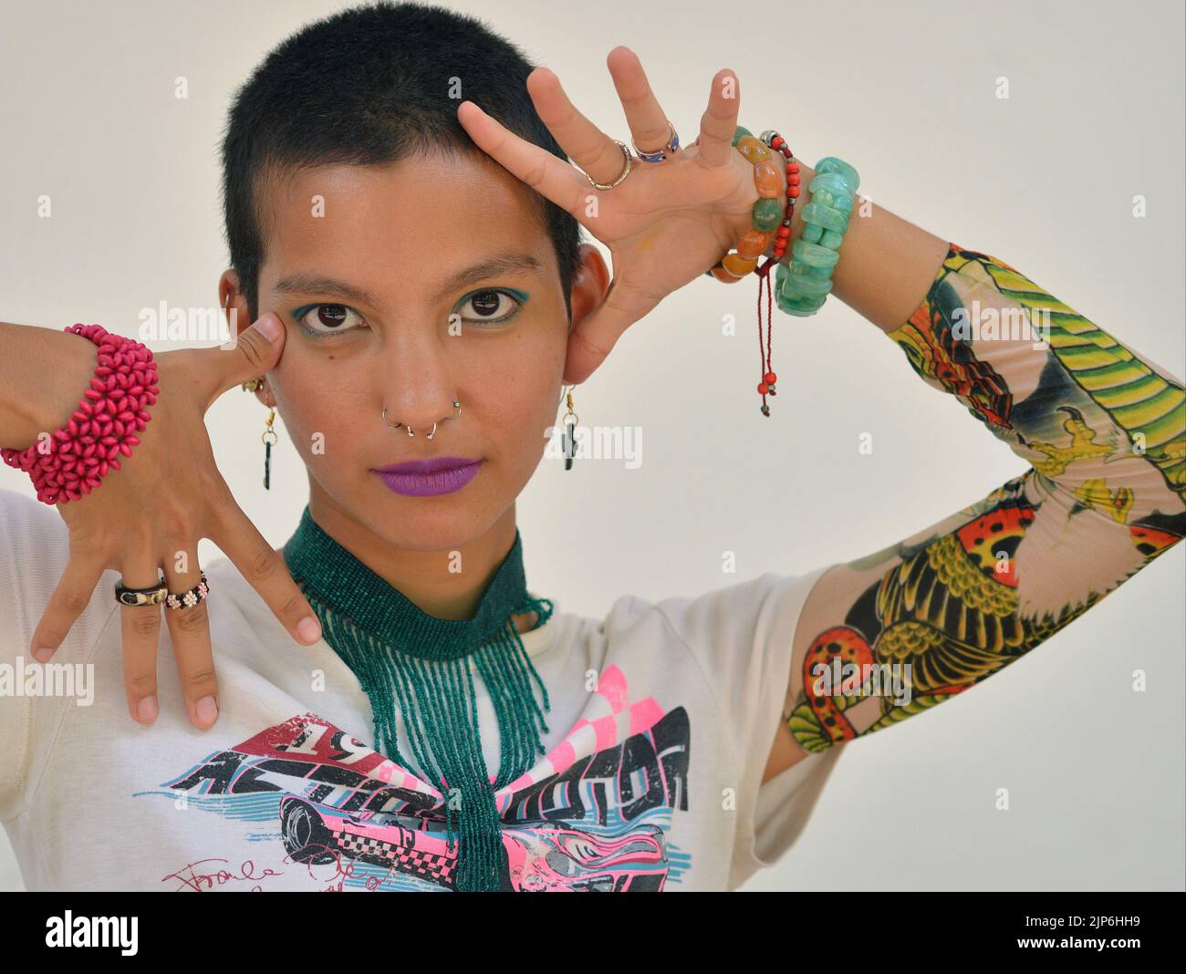 Jeune attrayant beau modèle mexicain femelle avec des cheveux très courts porte des manchons de protection de tatouage et pose avec des gestes expressifs créatifs de main. Banque D'Images