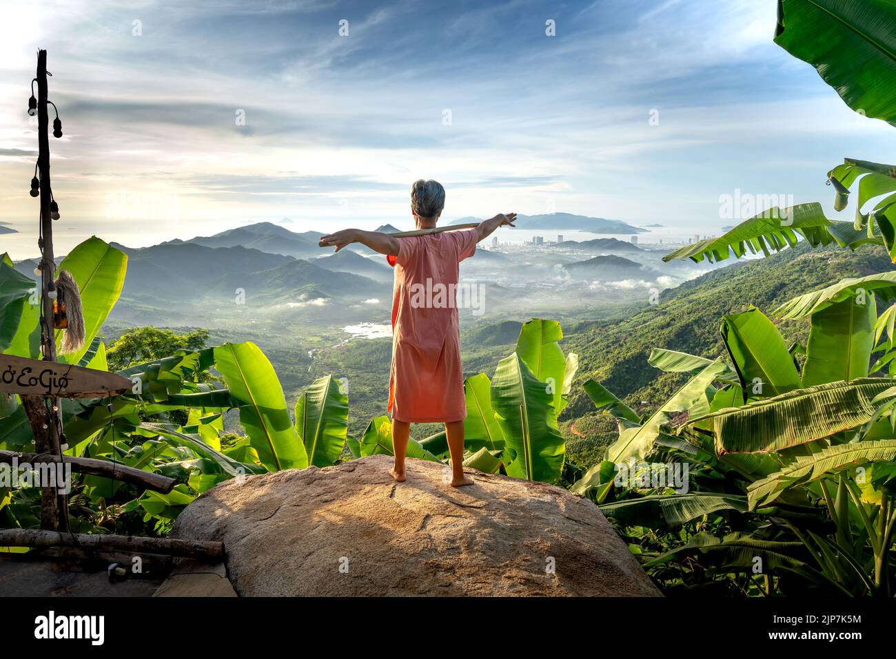 Femme âgée faisant des exercices matinaux avec un bâton dans les montagnes de Nha Trang. La ville côtière de Nha Trang se trouve au loin Banque D'Images