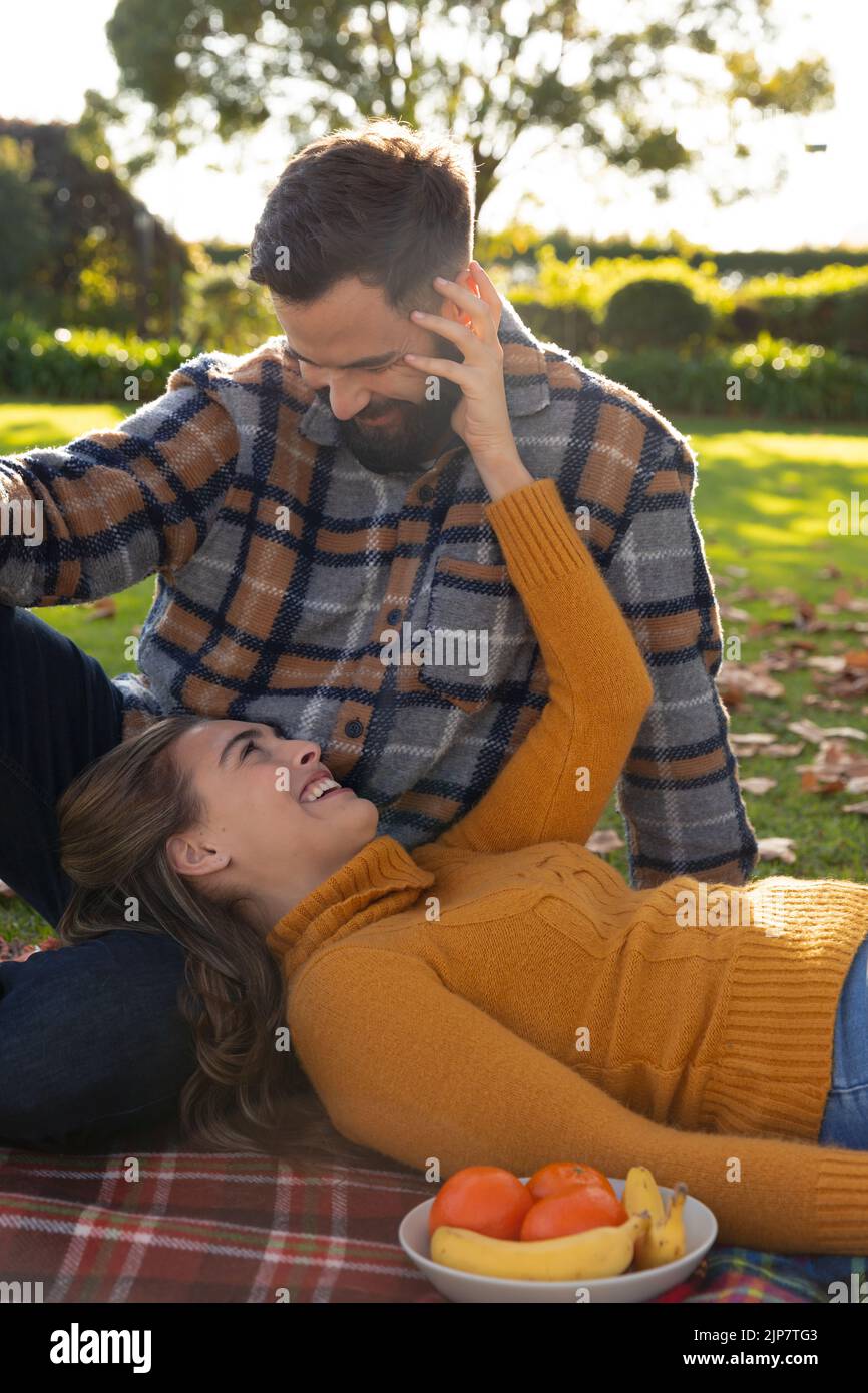 Couple caucasien romantique sur tapis ayant pique-nique et embrassant dans le jardin d'automne ensoleillé Banque D'Images