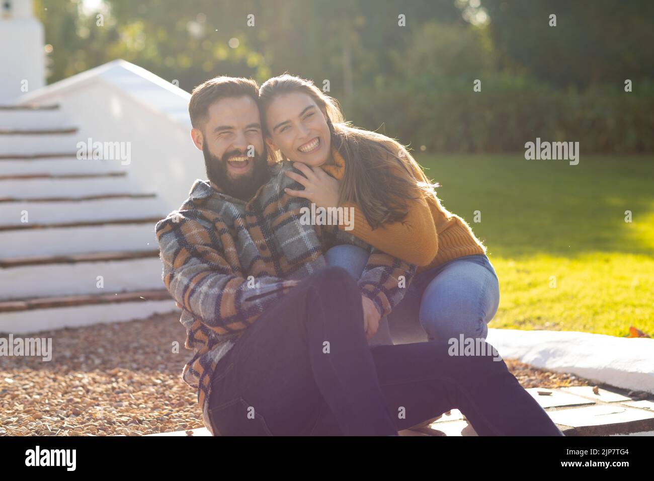 Portrait d'un couple caucasien assis sur des marches en terrasse riant et embrassant dans le jardin ensoleillé d'automne Banque D'Images