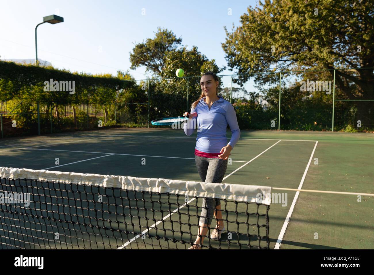 Femme caucasienne jouant au tennis rebondissant sur une raquette sur un court de tennis extérieur Banque D'Images