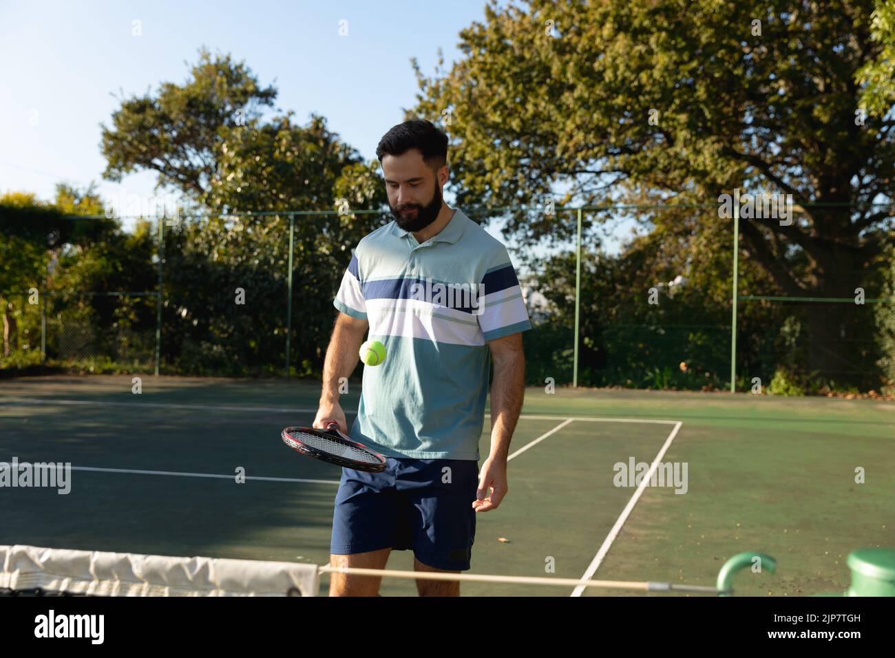 Homme caucasien jouant au tennis rebondissant sur une raquette sur un court de tennis extérieur Banque D'Images