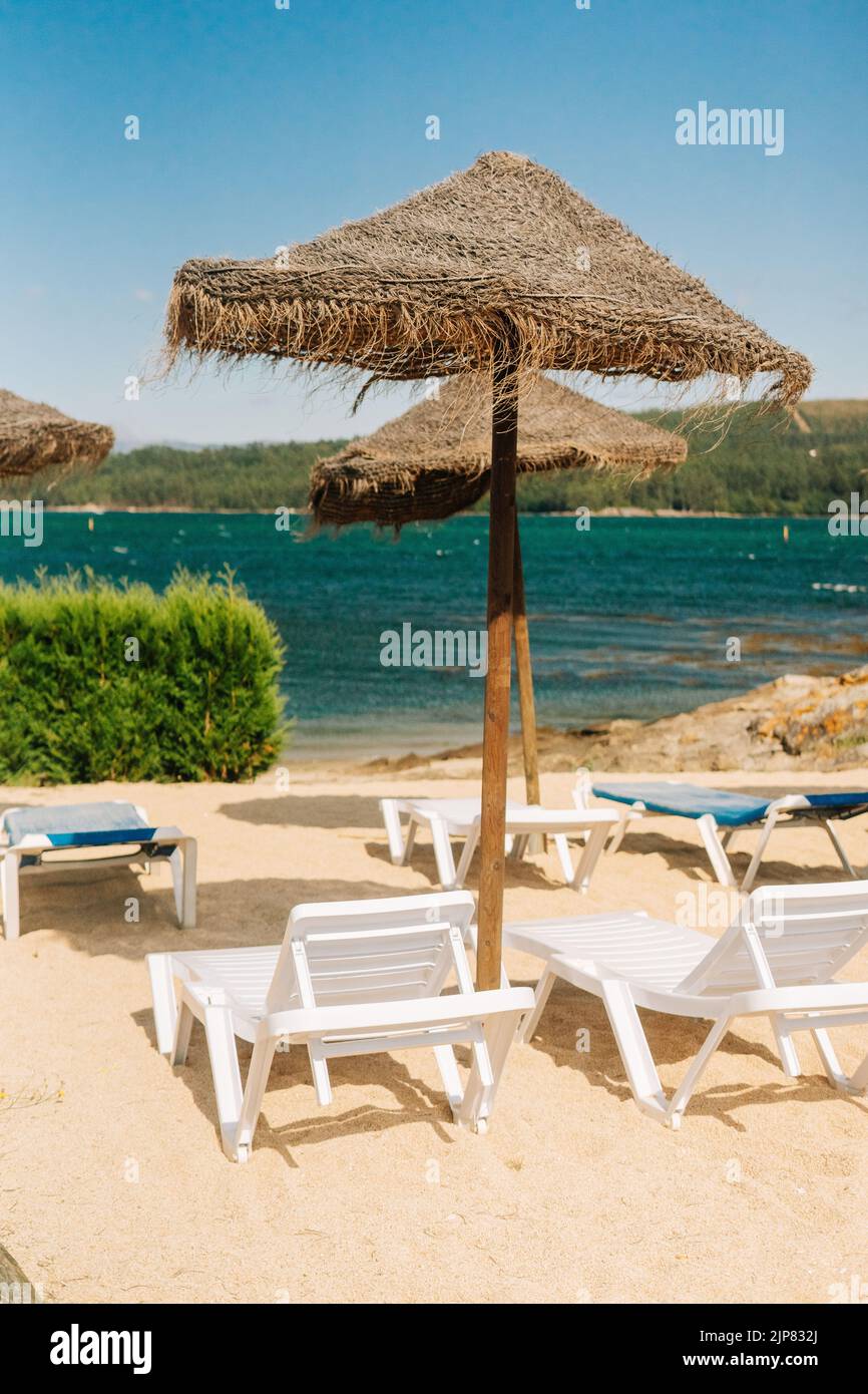 Chaises longues avec parasols en paille près de la rivière en Galice, Espagne Banque D'Images