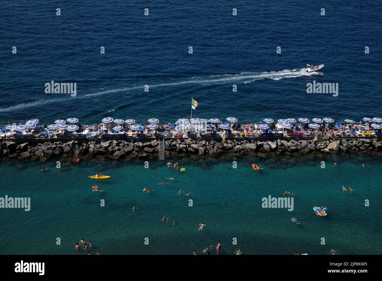 Club de plage privé à Sorrento, dans le sud de l'Italie, montrant des baigneurs de soleil assis sur le brise-lames et appréciant la mer. Banque D'Images