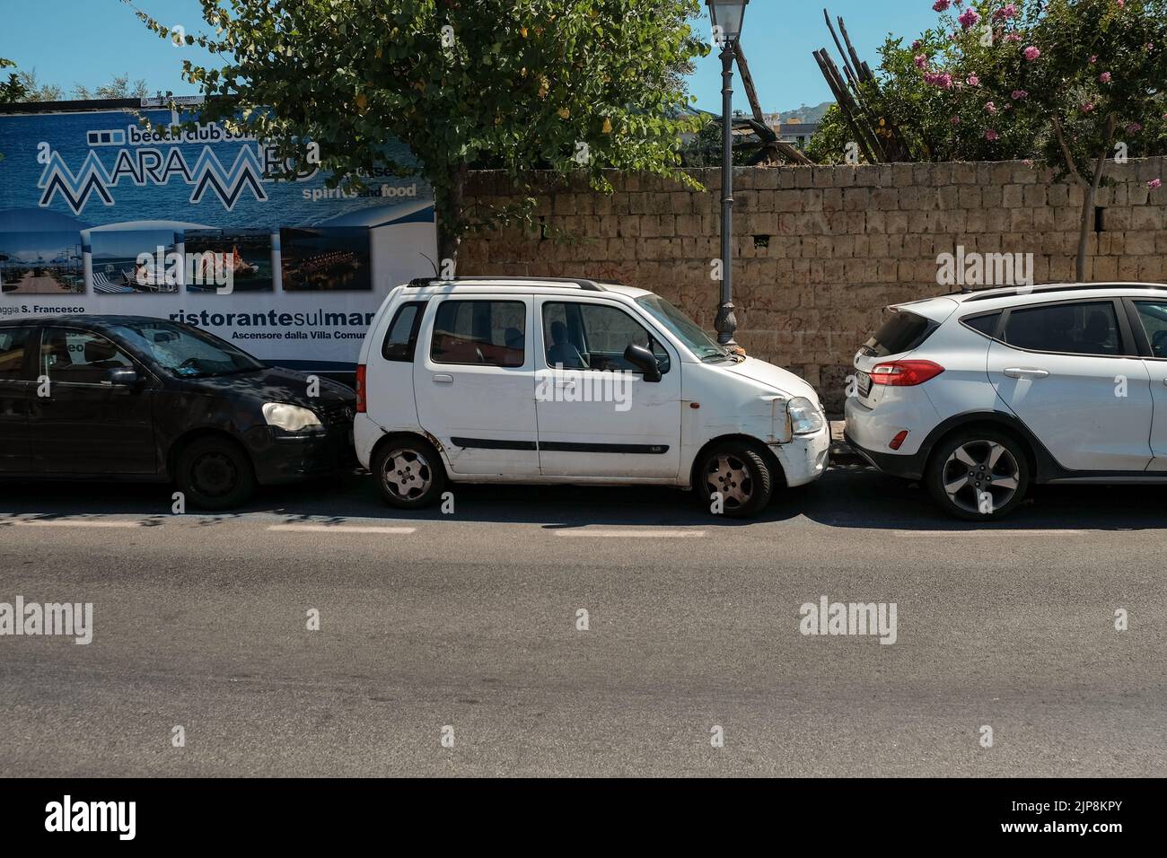 Parking très serré en Italie avec une petite voiture familiale bosselée pare-chocs à pare-chocs écrasé à côté de deux voitures dans une baie de stationnement avec seulement des pouces pour bouger. Banque D'Images