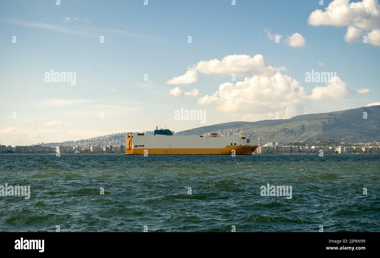 Bateau blanc et jaune naviguant sur la mer. Paysage urbain derrière lui avec ciel nuageux. Banque D'Images