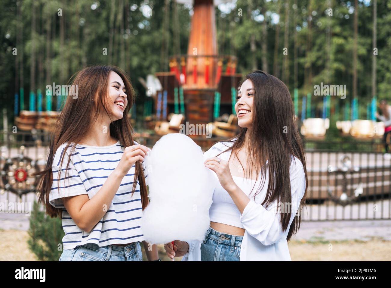 Jeunes femmes avec des amis à cheveux longs avec des bonbons de coton dans leurs mains ayant le plaisir au parc d'attractions Banque D'Images
