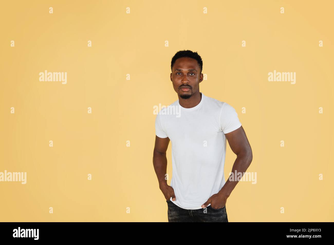 Portrait d'un jeune homme afro-américain attrayant, portant un t-shirt blanc, posant à l'appareil photo sur fond jaune pastel. People, races concept. Banque D'Images