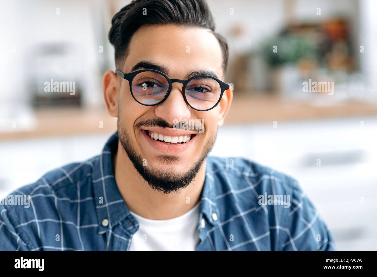 Gros plan d'un beau jeune homme de course mixte avec des lunettes, un indépendant ou un étudiant, dans une chemise décontractée, avec des dents blanches parfaites, regardant l'appareil photo avec un sourire joyeux et ensanglant Banque D'Images