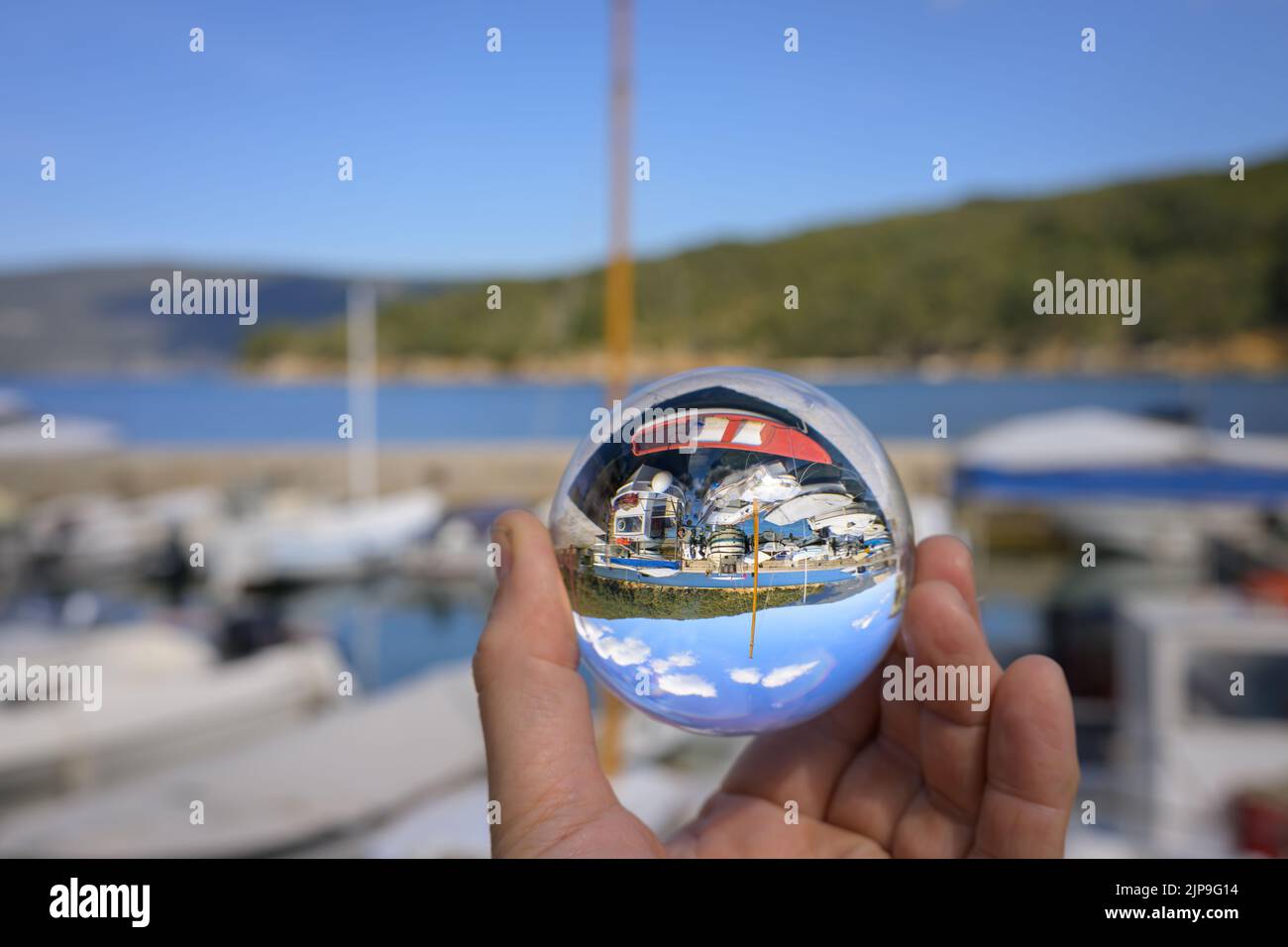 Main tenant la sphère de verre dans le petit port de Valun (Cres, Croatie), jour ensoleillé au printemps Banque D'Images