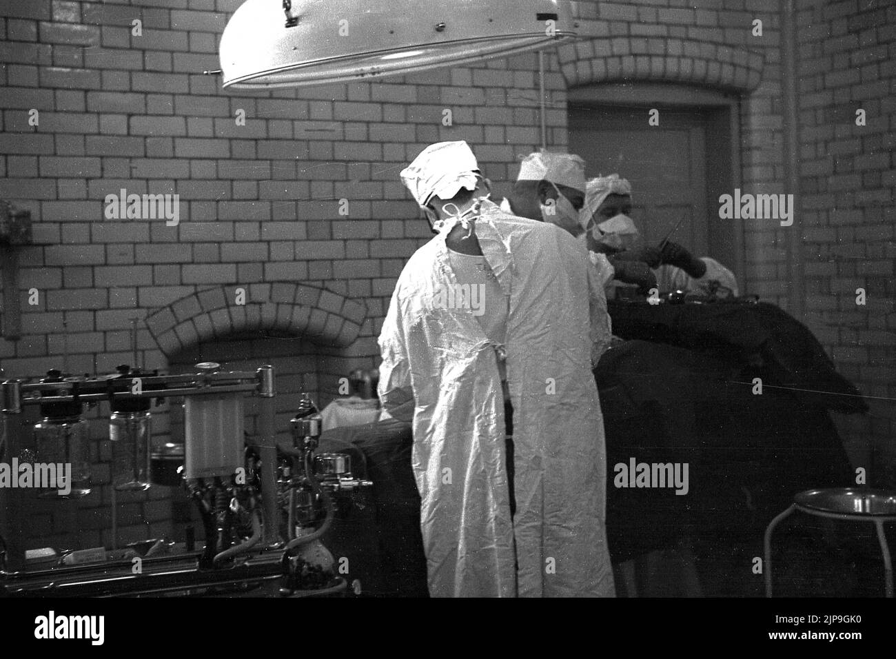 1953, historique, à l'intérieur d'un bloc opératoire, deux chirurgiens au travail effectuant une chirurgie sur un patient, Angleterre, Royaume-Uni. Banque D'Images