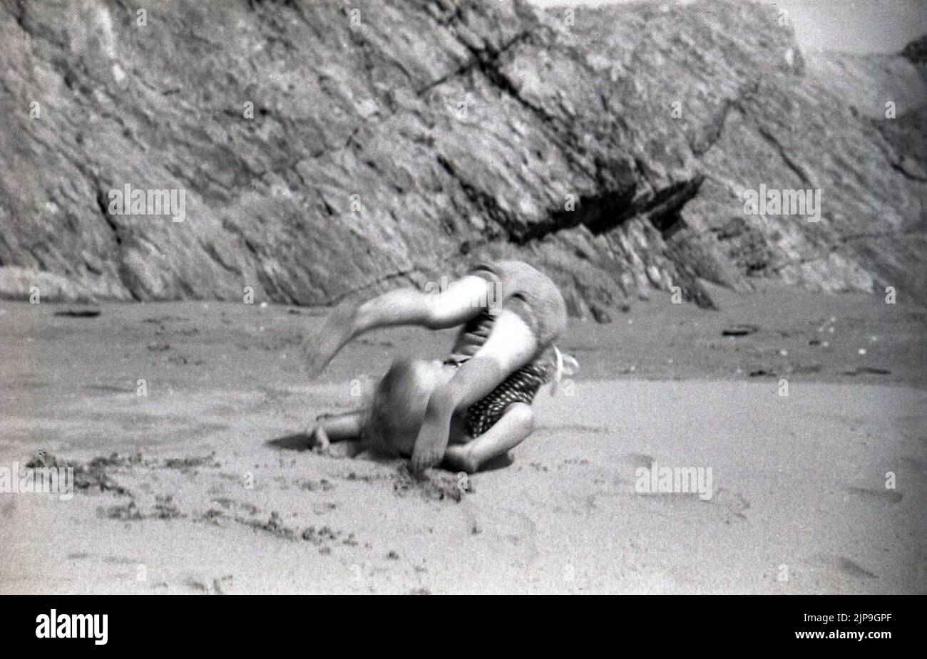 1950, bébé garçon faisant un rollover sur une plage de sable, Angleterre, Royaume-Uni. Banque D'Images