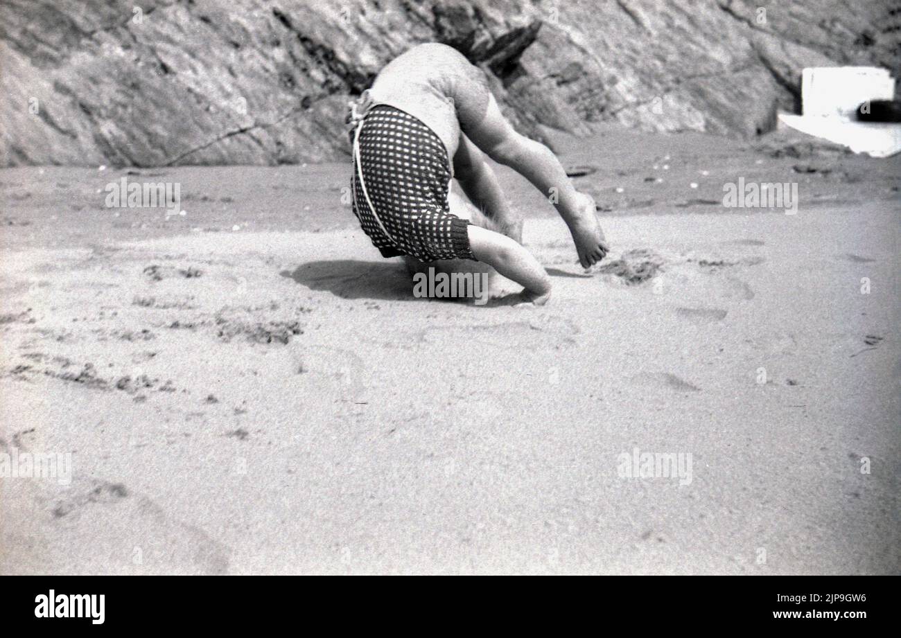 1950, bébé garçon faisant un rollover sur une plage de sable, Angleterre, Royaume-Uni. Banque D'Images